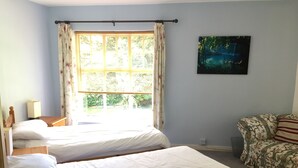 Een kamer met twee eenpersoonsbedden, een houten nachtkastje met een lamp, een bank met bloemenprint en een schilderij van een boslandschap.