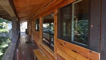 A wooden cabin with a covered porch, large windows, and a view of a forested area.