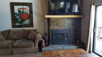A living room with a stone fireplace, a television mounted above it, and a painting on the wall.