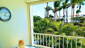 A balcony with a table featuring lemon slices and a pineapple, overlooking a garden with palm trees and a building in the background.