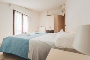 Two beds with crisp bedding, a wardrobe, and a bedside table with a lamp, set in a well-maintained room.