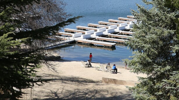 Une vue sur le lac, avec des bateaux amarrés, une plage de sable et une forêt environnante.