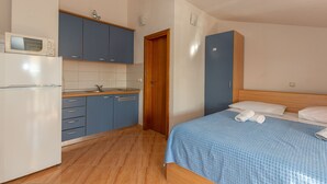 Una habitación compacta con cama, una kitchenette pequeña y una puerta de madera.