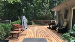 Un terrazzo in legno con mobili da esterno, una zona coperta e vista su una zona boschiva.