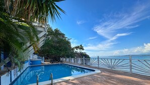 A pool with a wooden deck and a white fence overlooking a body of water.