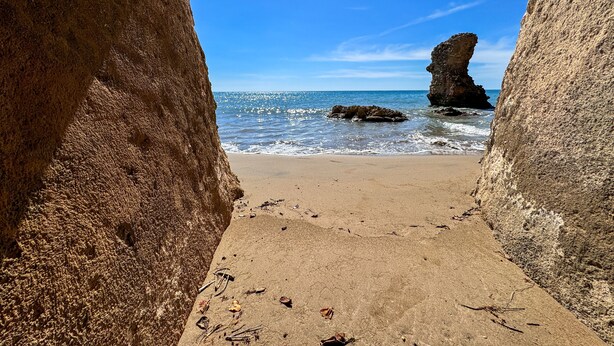 A beach view through a rocky archway with a clear blue sky and ocean.