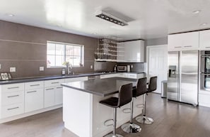 A modern kitchen with a central island, bar stools, stainless steel appliances, and a large window providing natural light.