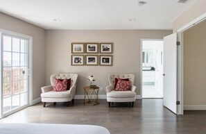 A spacious room with two armchairs, a small side table with a vase, and a wall with framed pictures.