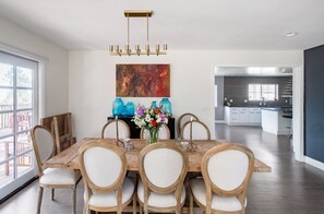 A dining area with a wooden table and chairs, a vase of flowers, and a chandelier.