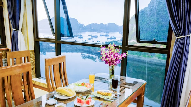 Una mesa de comedor con sillas, un jarrón de flores y una vista de barcos en el agua a través de grandes ventanales.