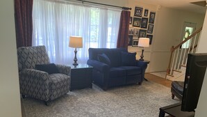 A living room with patterned armchairs, a blue sofa, and a rug. There are two lamps on side tables, and a staircase is visible in the background. - Clean, Spacious Family House (Annapolis)
