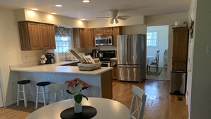 A modern kitchen with wooden cabinets, stainless steel appliances, and a central island with bar stools. - Clean, Spacious Family House (Annapolis)