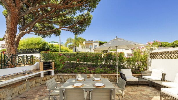 An outdoor patio with a stone floor, a dining table set with plates and cutlery, and a seating area with wicker furniture. - CASAS DA PRAIA JOANA (Almancil)