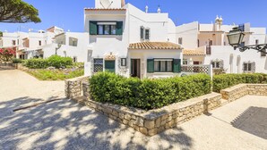A white building with green shutters, a stone pathway, and a small garden area. - CASAS DA PRAIA JOANA (Almancil)
