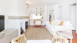 A spacious living room with a white sofa, wicker chairs, a flat-screen TV, and a fireplace. - CASAS DA PRAIA JOANA (Almancil)