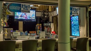 Una zona de bar con un letrero que ofrece dos por uno en cervezas de barril entre las 4 y las 7 de la tarde, un televisor mostrando deportes y un letrero de neón publicando bebidas especiales.