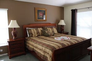 A neatly made bed with a striped bedspread, two bedside tables with lamps, a framed picture on the wall, and a window with curtains. - 3 MILLES FROM DISNEY, GATED SECURITY RESORT,GAMES IN PLACE. (Kissimmee)