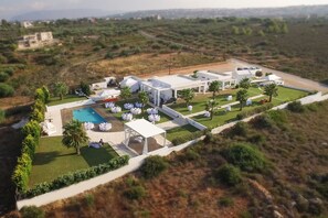 An aerial view of a resort with a swimming pool, white tents, and palm trees. - ktima reveli luxury villa (χανια καλαθας)