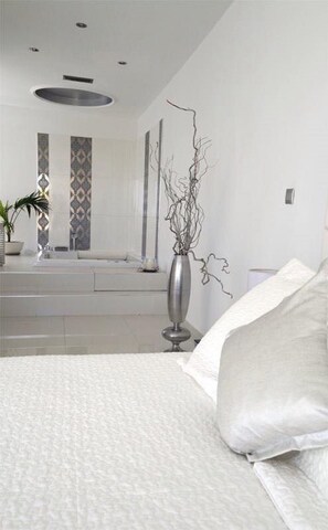 A modern bedroom with a large bed, a vase with branches, and a bathroom in the background. - ktima reveli luxury villa (χανια καλαθας)