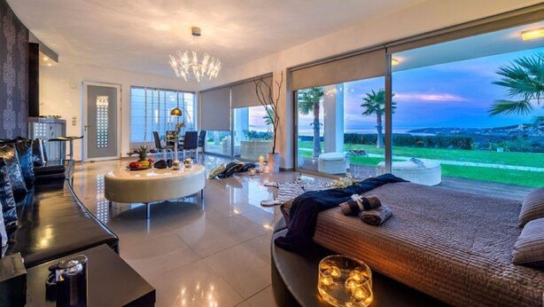 A modern bedroom with a large bed, a sitting area with a coffee table, and a view of the outdoors. - ktima reveli luxury villa (χανια καλαθας)