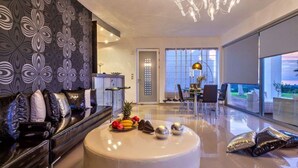 A modern living room with a round coffee table, a sofa, and a dining area with chairs. There is a large window with a view of the outdoors. - ktima reveli luxury villa (χανια καλαθας)