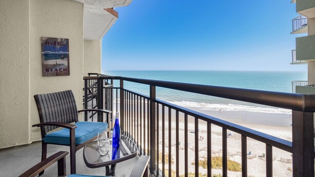 A balcony with a view of the beach, a chair, a table with a glass, and a bottle. - Cozy 1Br Oceanview Suite/2 Balconies (Myrtle Beach)
