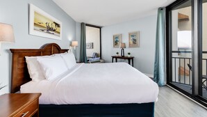 A hotel room with a large bed, a wooden headboard, a bedside table, a nightstand, two wall-mounted lamps, and a large window with a view of the outside. - Cozy 1Br Oceanview Suite/2 Balconies (Myrtle Beach)
