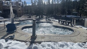 A snow-covered outdoor area with a hot tub, benches, and a stone wall.