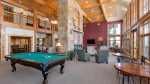 A spacious indoor area with a pool table, comfortable seating, and a stone fireplace.