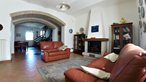 A spacious living room with a fireplace, leather sofas, a dining area, and a staircase leading to another level. - Il Poggio dell'Artilla, an oasis of peace to relax and regenerate (castiglione in teverina  (VT) Lazio)