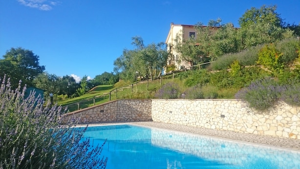 A swimming pool with stone walls, surrounded by greenery and a house in the background. - Il Poggio dell'Artilla, an oasis of peace to relax and regenerate (castiglione in teverina  (VT) Lazio)