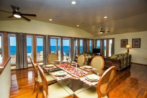 A dining area with a table set for six, large windows, and a view of the ocean.