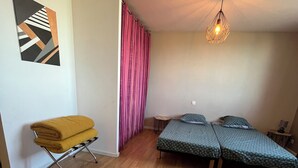 Een kamer met een houten vloer, een bed met behang, een gele stoel, een tafeltje en een hanglamp.