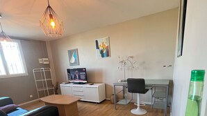Een moderne woonkamer met houten vloer, een zwarte bank, een wit bureau, een televisie en een hanglamp.