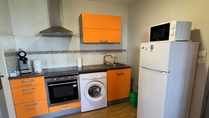 Een compacte keuken met een wasmachine, oven, magnetron en een kleine koelkast.