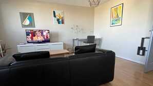 Een moderne woonkamer met een zwarte hoekbank, een flatscreen televisie, houten vloeren en abstracte wanddecoratie.