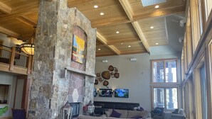 A spacious living area with a stone fireplace, wooden ceiling beams, and a large window. - One Bedroom Master Unit. Beautiful Luxury Ski in, Ski Out Resort (Breckenridge)