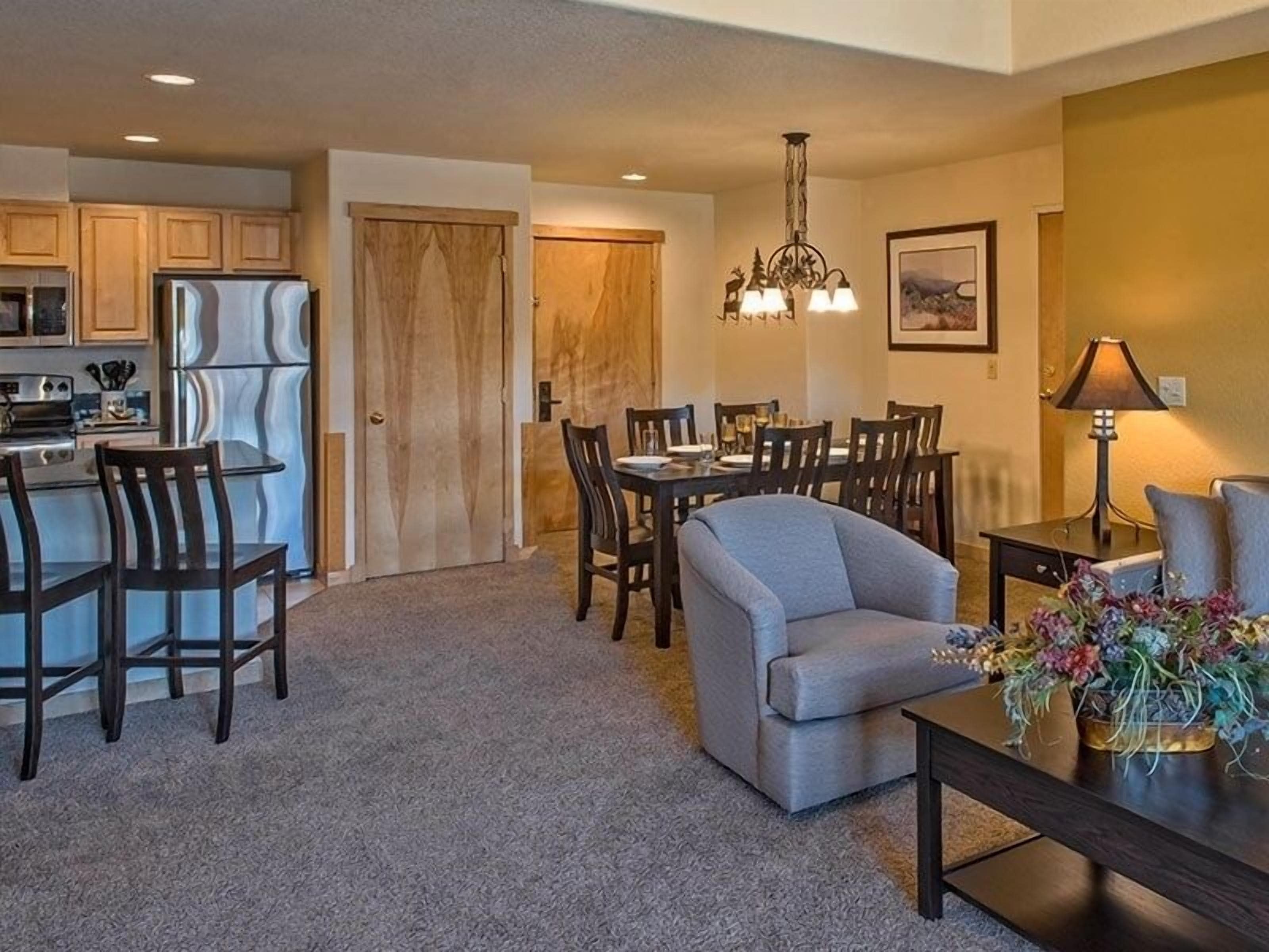 A modern kitchen with a refrigerator, stove, and microwave. There is a dining area with a table and chairs, and a living room with a sofa and a coffee table.