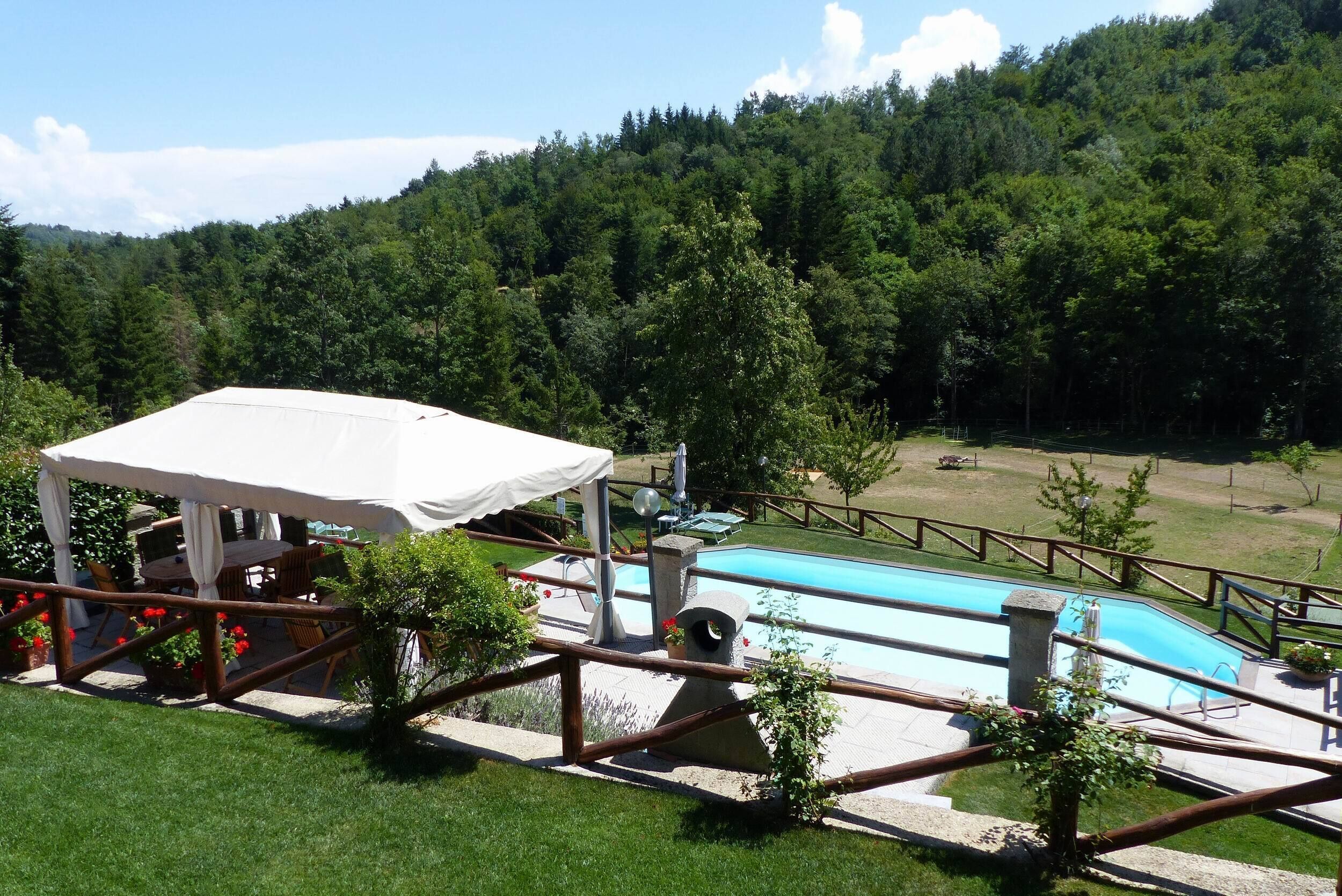 Ein Poolbereich mit Holzterrasse, überdachter Sitzgelegenheit und Blick auf einen bewaldeten Hügel.