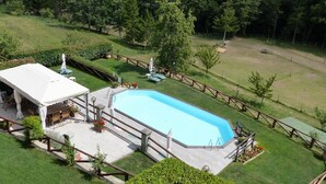 Una piscina con zona de deck, rodeada por una valla de madera y vegetación.