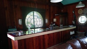 A wooden interior with a bar area, a sofa, and a large window with a decorative glass design.