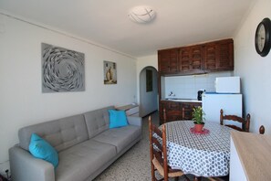Un espacio habitable compacto con sofá, mesa de comedor con sillas, zona de cocina con armarios y refrigerador, y un reloj de pared.