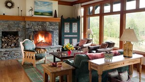 Una sala de estar acogedora con chimenea de piedra, asientos cómodos y ventanas amplias con vistas al exterior.