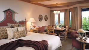 Habitación de hotel con una cama grande, una mesa de comedor, una silla, una mesita con un florero y vistas al exterior.