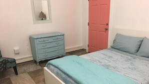 Un dormitorio con cama, cómoda, puerta y una silla.