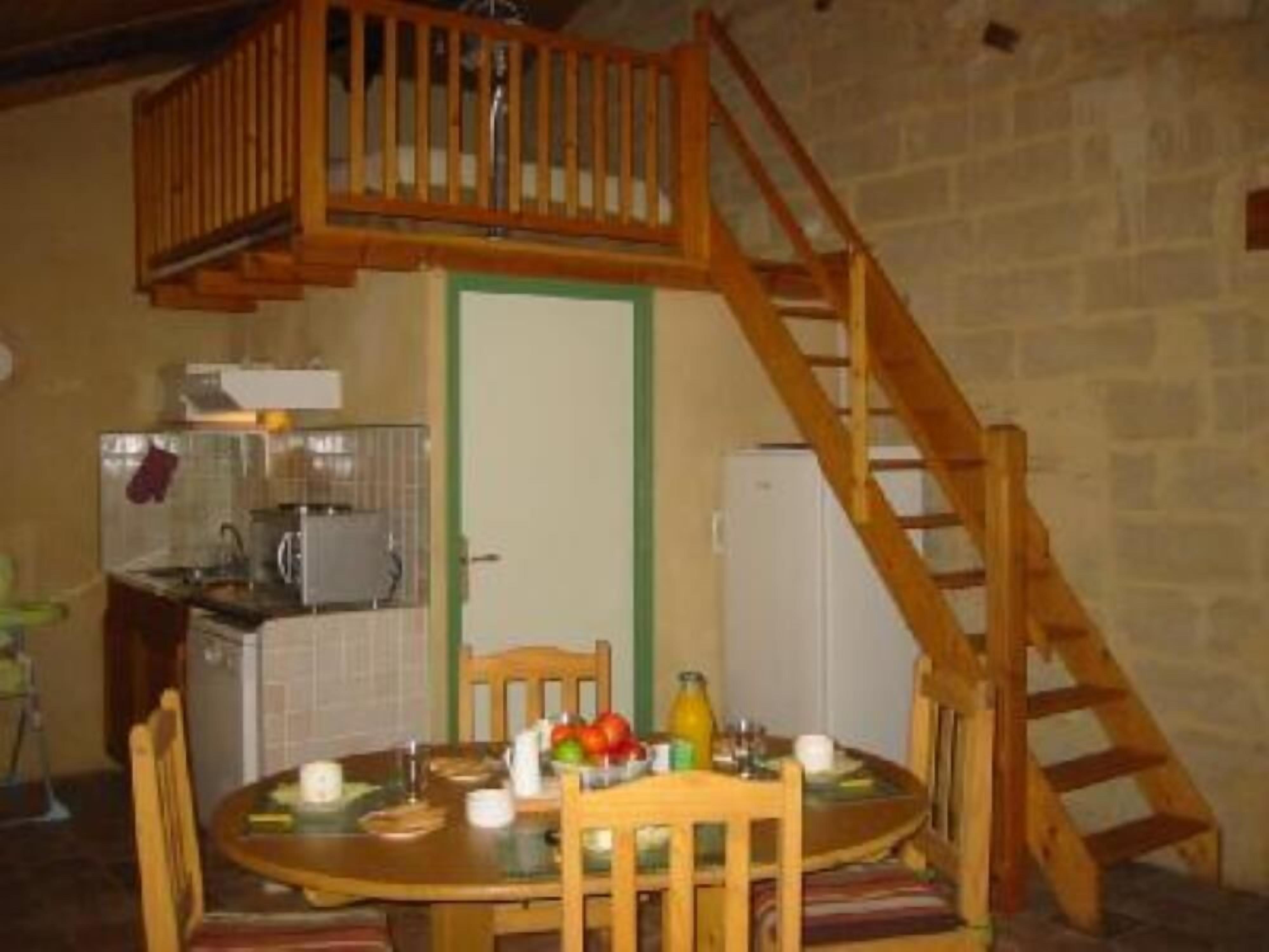 Ein Essbereich mit Holztisch und Stühlen, im Hintergrund eine Küche und eine Holztreppe.