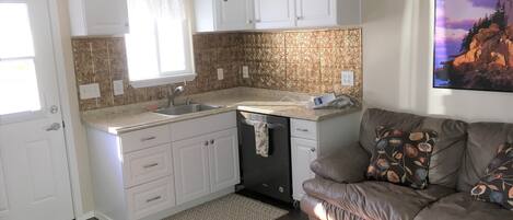 A compact kitchen with white cabinets, a built-in dishwasher, and a window above the sink.
