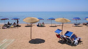 Ein Strand mit Liegestühlen und Sonnenschirmen, ein klarer Himmel und das Meer im Hintergrund.