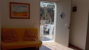 Ein Zimmer mit einem gelben Sofa, einem gerahmten Landschaftsbild und einer Glastür zum Außenbereich.