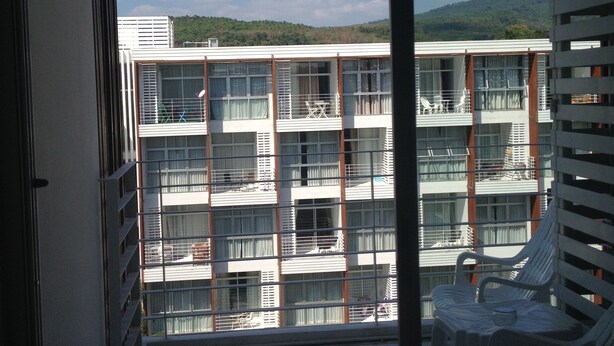 A balcony with a view of a multi-story building, a chair, and a tiled floor. - Nice 1- Bedroom Condo In Klong Muang (Klong Muang)